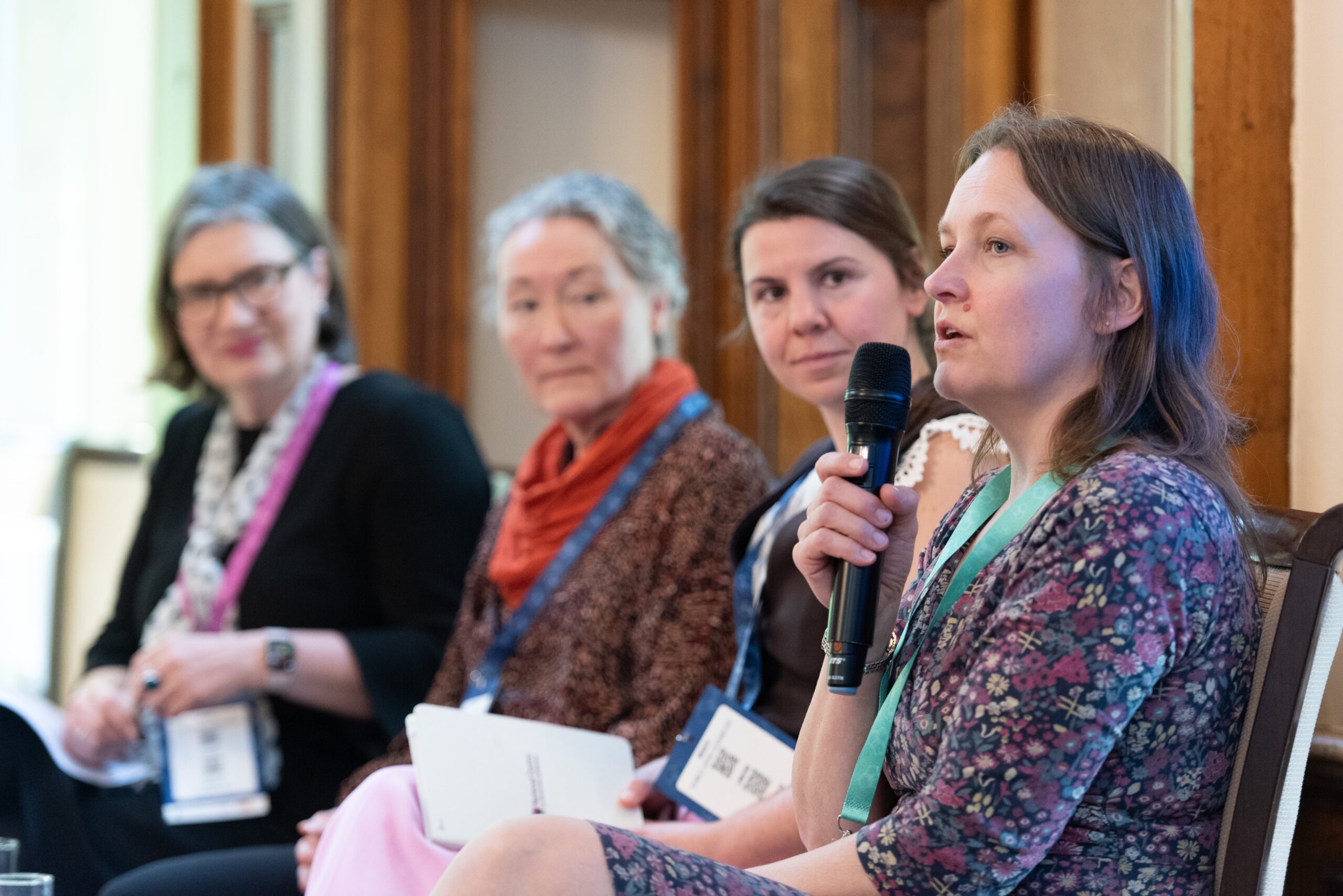 Liz Collins, Executive Director of Pharmaceutical Sciences at Pfizer, speaks into a microphone at the Developing Business-Aware Academics launch event. Behind her are sat Flora Hamilton, Paula Whitehouse, and Danielle Croucher