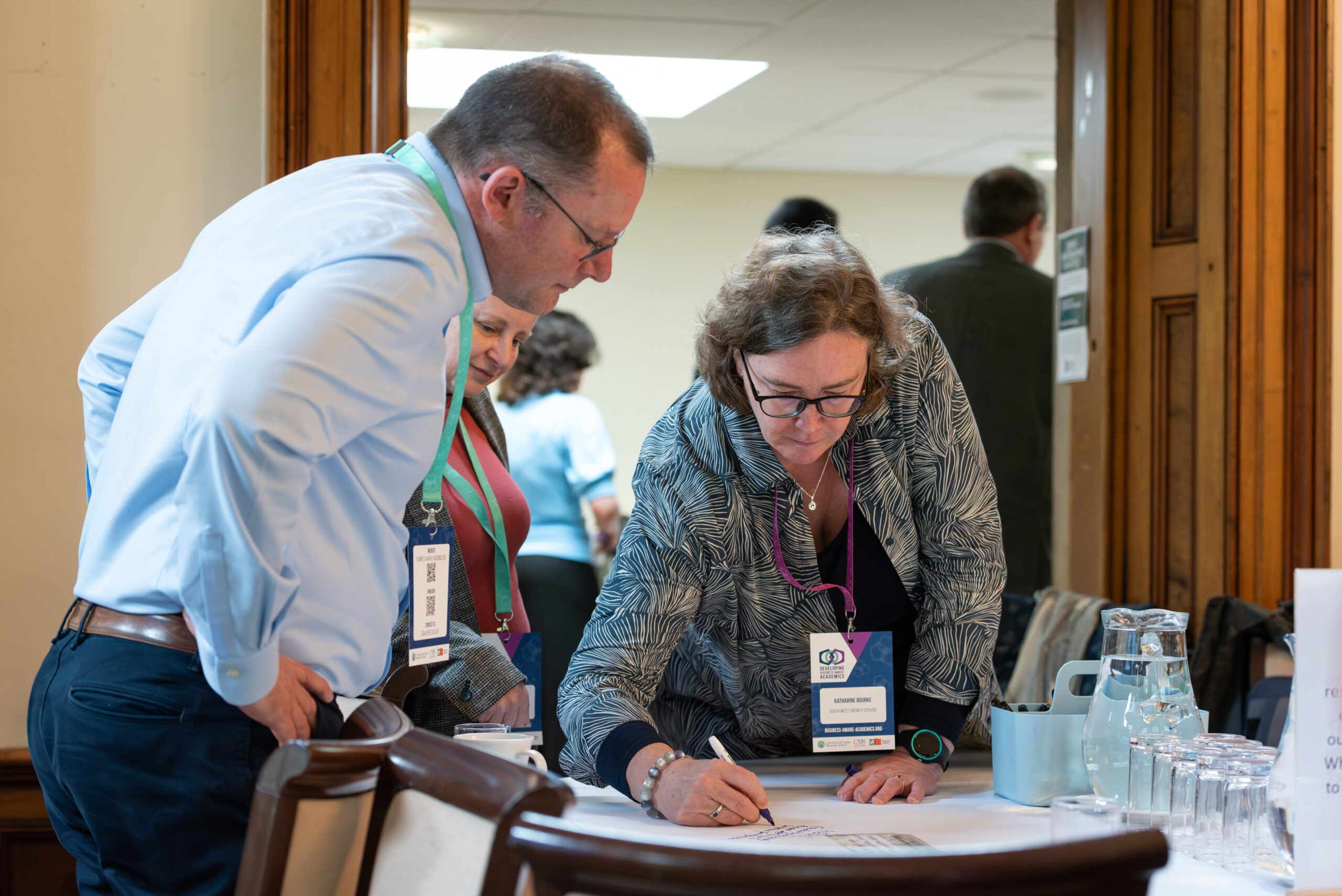 A woman leans over a table to write while two people watch at the Developing Business-Aware Academics launch event