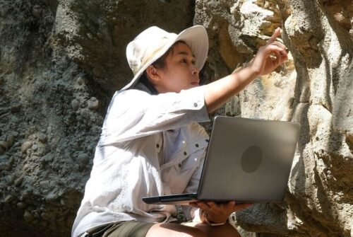 an archaeologist examines a rock sample using a laptop computer