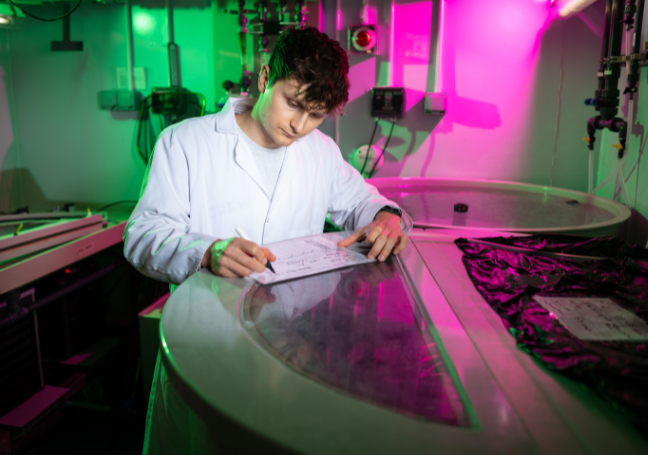 A photo of PhD researcher Jack Jarvis, writing on top of a large cylindrical tank