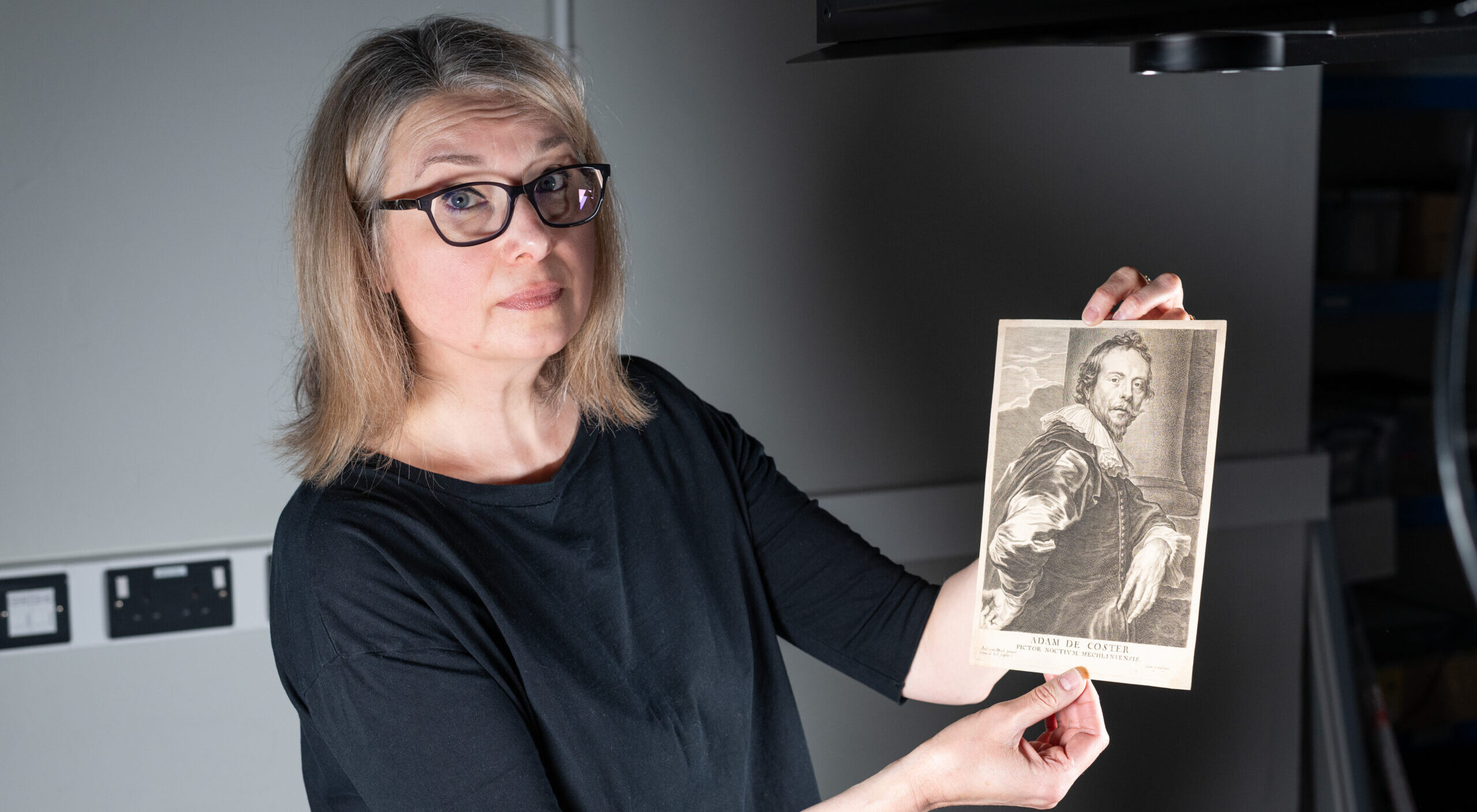 A photo of Dr Meredith Hale, holding up a small print of a portrait painting