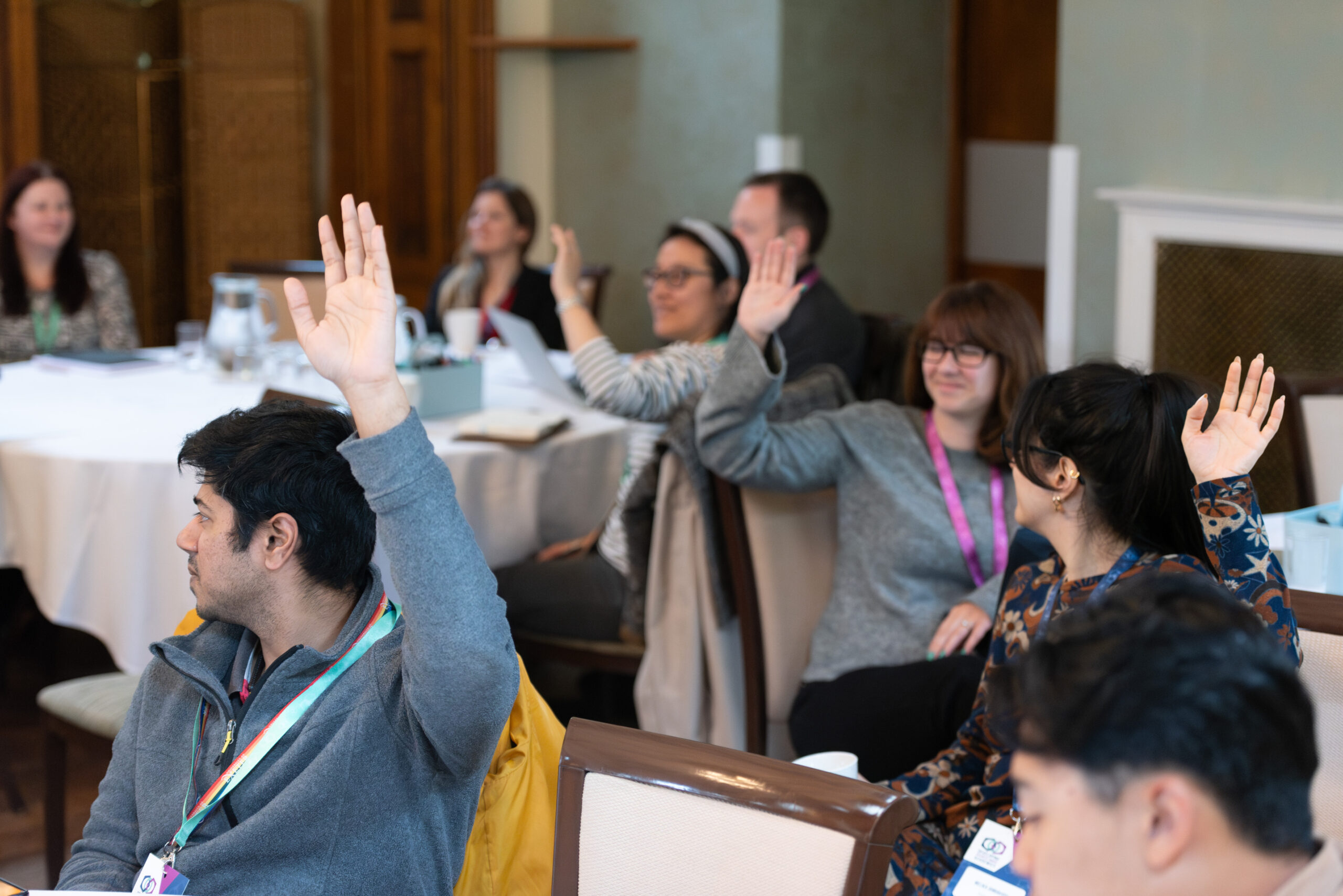 A photo of three groups of people in round table discussions. A number of the people have raised their hands